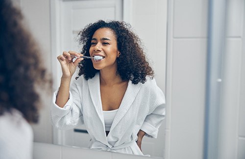 Woman in white robe brushing her teeth in bathroom