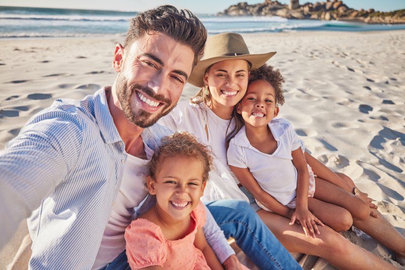 Patient smiling with family on the beach after preventing dental emergencies